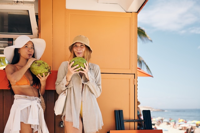 Two women drinking fresh coconut water on a sunny beach.