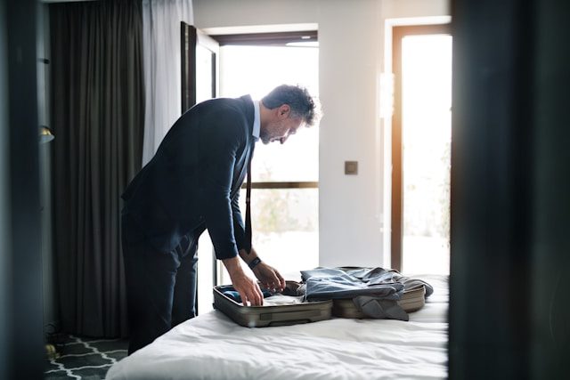 A businessman in a suit packing his travel bag in a bright hotel room, carefully arranging his belongings.