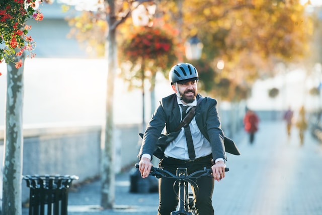 Businessman in a suit riding an ebike on a city street, commuting to work on a sunny day.