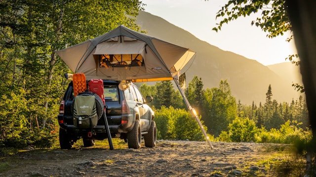 A car equipped with a rooftop tent parked in a scenic area with mountains in the background at sunset.