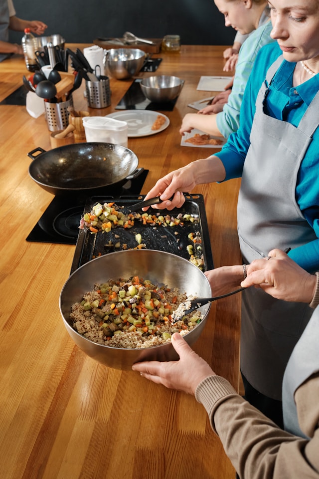 An instructor in a cooking class helping students prepare a vegetarian dish, featuring a mix of colorful vegetables being stirred in a bowl, in a well-equipped kitchen environment.