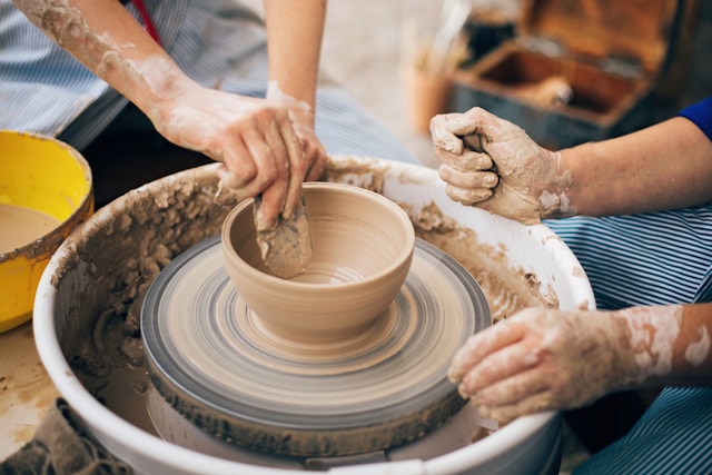 Two people in a pottery workshop working on a bowl in a pottery wheel