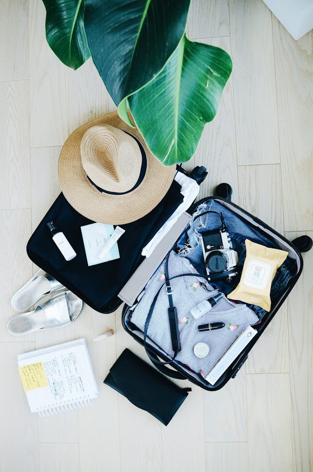 Top view of a suitcase with a variety of travel items including a hat, toiletries, clothes, and a notebook.