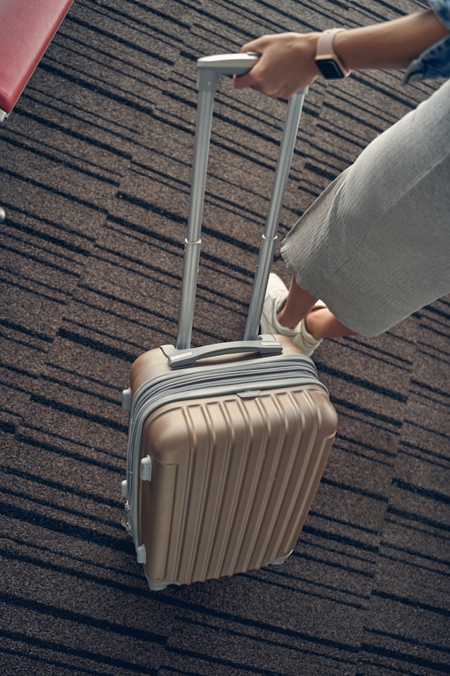 Traveler pulling a beige hard-shell carry-on suitcase through an airport, ready for departure.