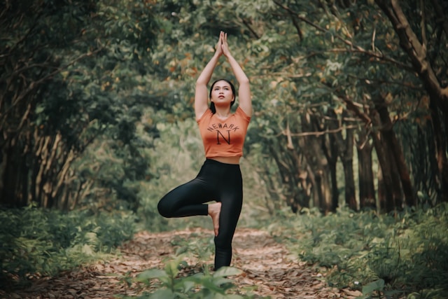 Woman practicing Tree Pose in a serene forest setting, demonstrating balance and tranquility.