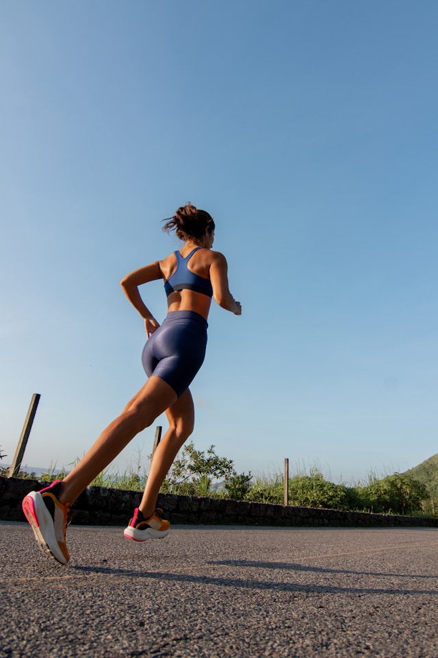 A woman in blue athletic gear running on a road with scenic greenery and clear skies, exemplifying fitness and travel.