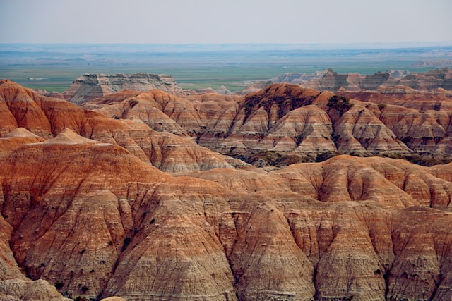 Aerial perspective of the layered rock formations and deep gorges of Badlands National Park, under overcast conditions.