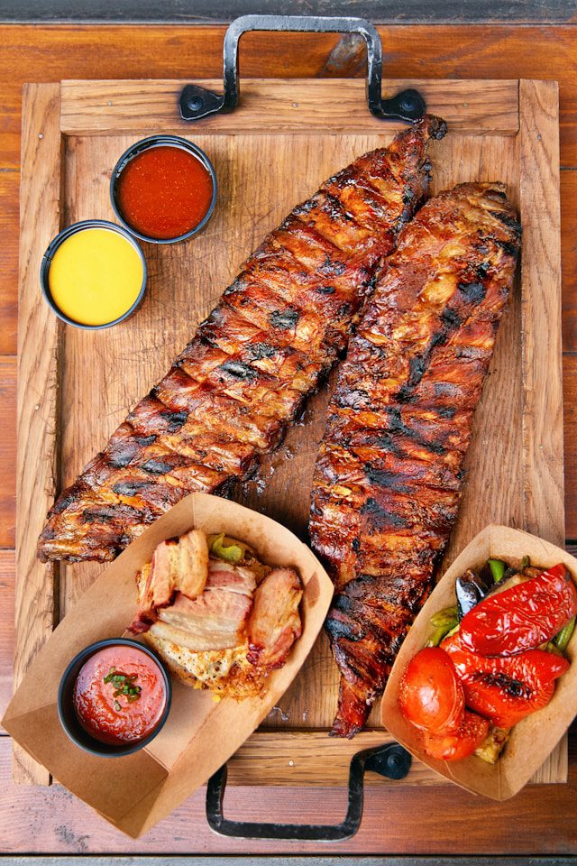 BBQ ribs platter with accompanying sauces and roasted vegetables, showcasing a mouthwatering BBQ feast.