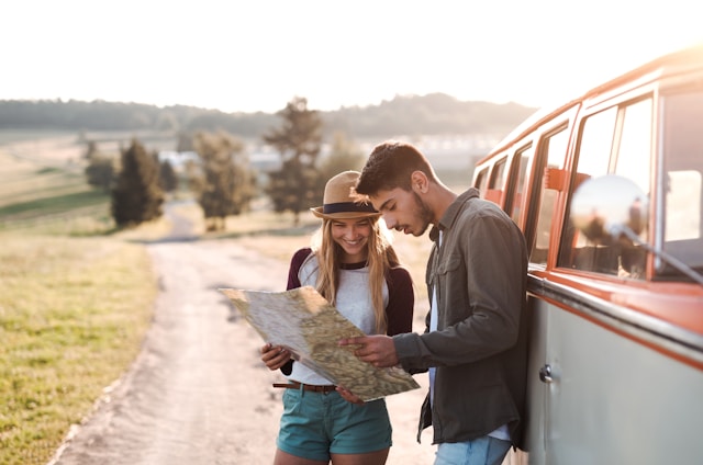 A young couple with a map planning their road trip beside a vintage red van in early morning light