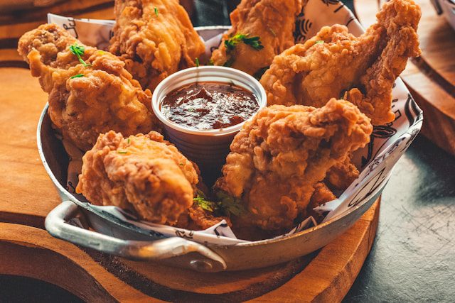 A basket of crispy fried chicken with a side of dipping sauce, served in a casual setting.