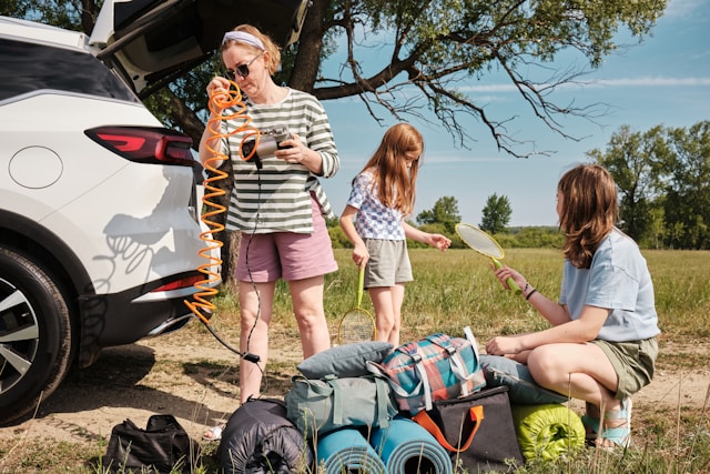 A family unpacking sports equipment and bags from their car during a road trip in a grassy field