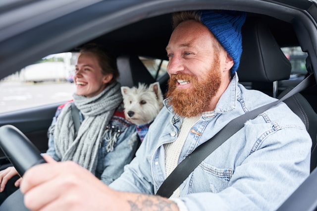 A happy couple with their white dog enjoying a car ride, smiling and laughing together