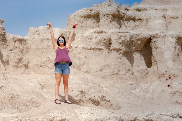 Woman with arms raised in celebration standing on the eroded terrain of Badlands National Park, South Dakota, showcasing the park's unique landscape.