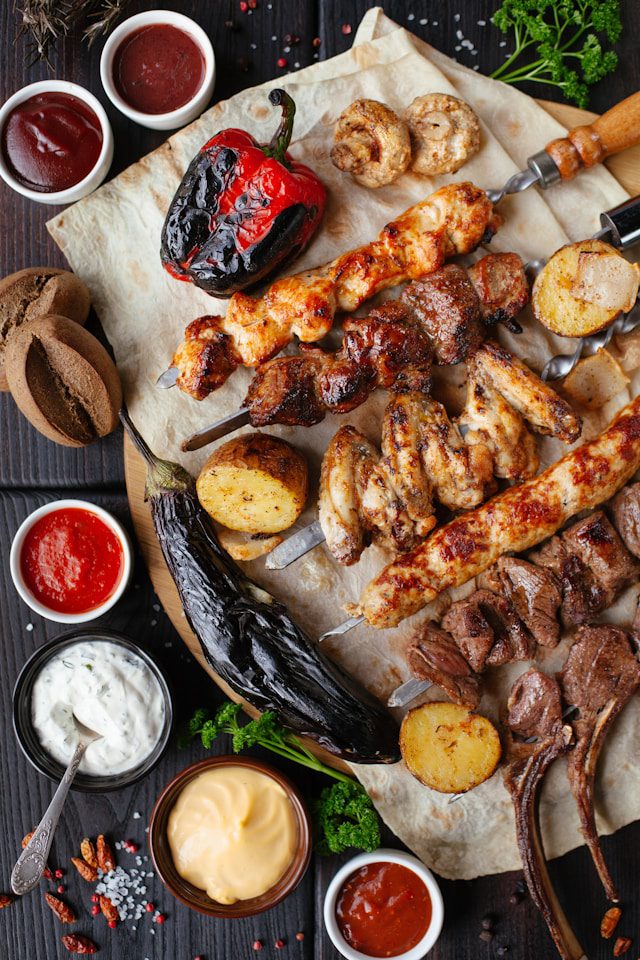 A hearty mixed grill platter featuring kebabs, grilled vegetables, and a variety of dips, arranged appealingly on parchment paper.