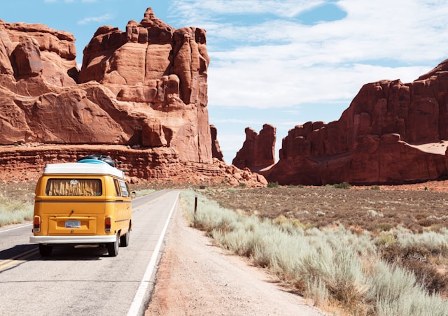 A bright yellow van driving through a scenic red rock canyon on a sunny day