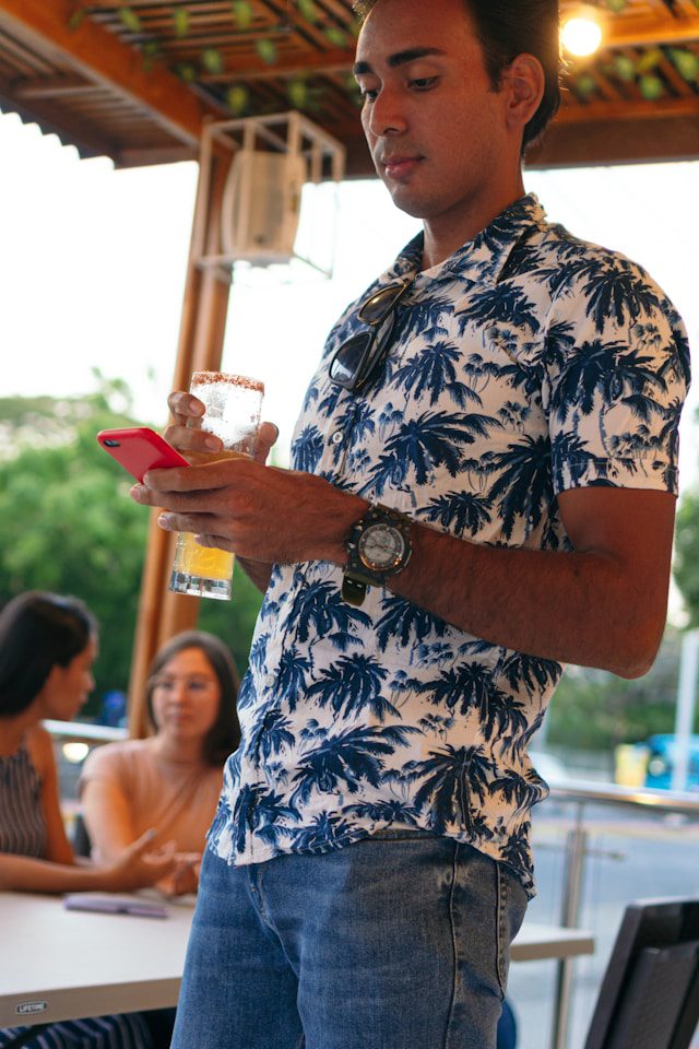 Young man checking his phone while holding a cocktail at an outdoor bar