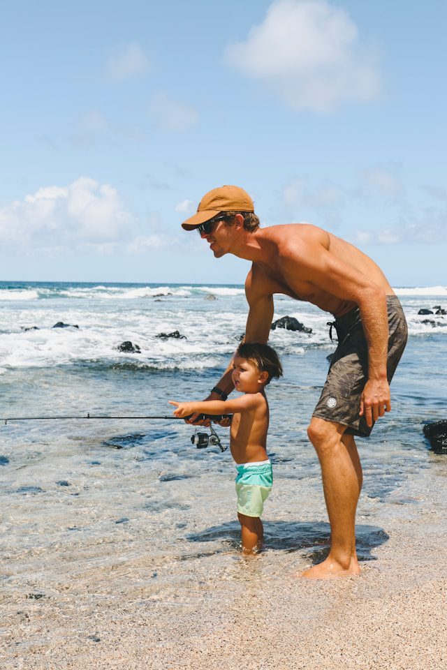 Father teaching his young son to fish on a rocky shoreline