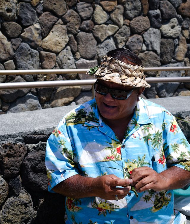 Local Hawaiian man in a traditional woven hat smiling while holding a cellphone