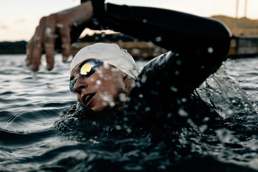 Woman swimming in open water wearing goggles and a swim cap at dusk.