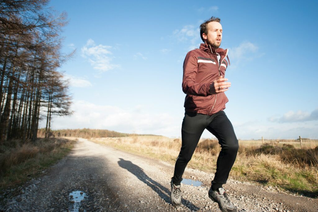 Man running on a rural country road with a backdrop of a clear sky and scattered trees.