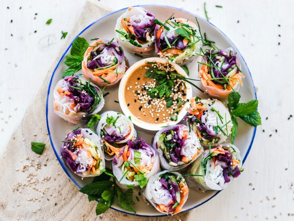 Fresh Vietnamese spring rolls filled with purple cabbage, carrots, and herbs, served with peanut dipping sauce on a blue-rimmed plate.