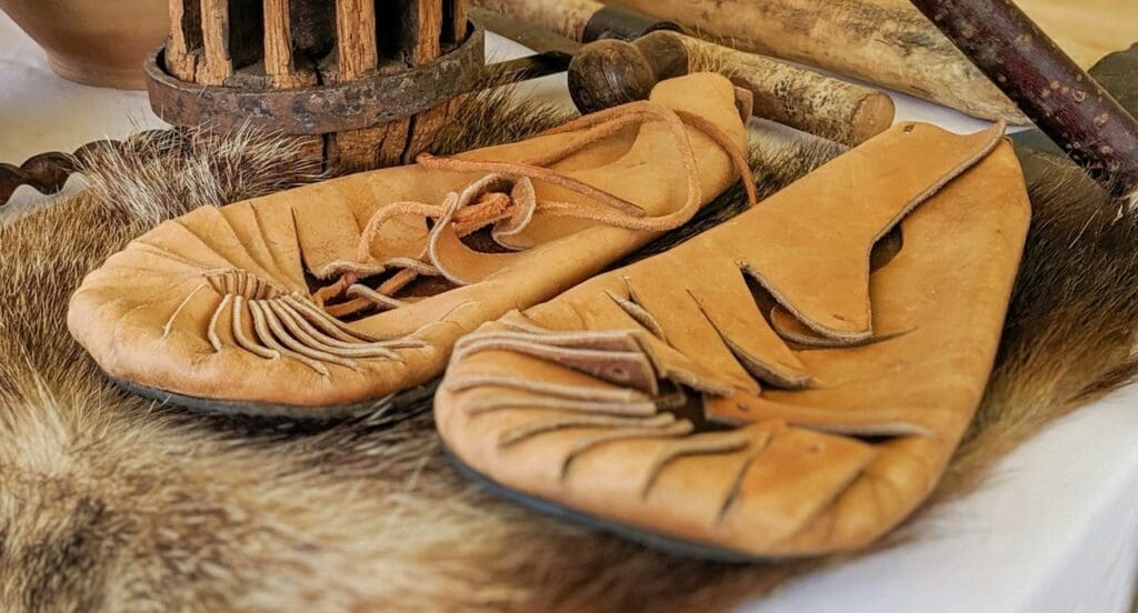 A display of ancient crafts on a table featuring leather moccasins set against a natural backdrop.