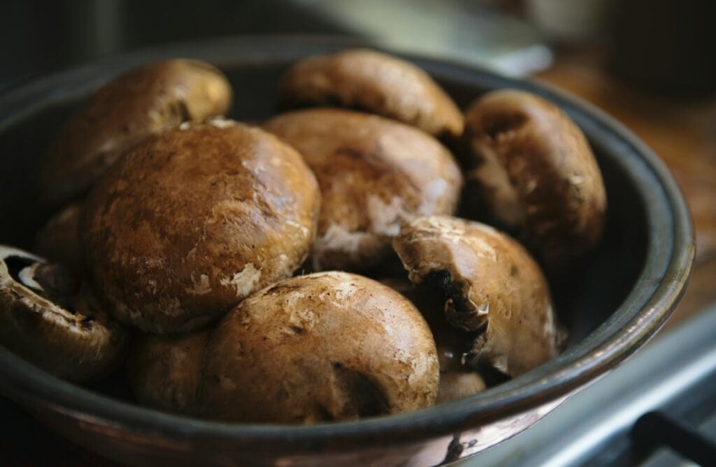 A group of whole crimini mushrooms in a rustic bowl, showcasing their rich brown caps and thick stems.