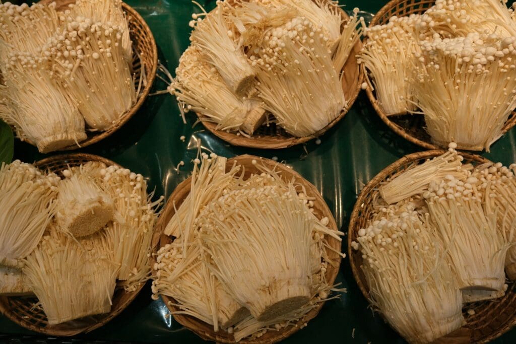 Several baskets filled with enoki mushrooms displayed on a green surface, showcasing their long thin stems and small caps.