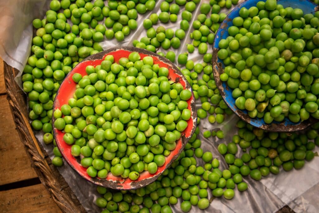 Fresh green peas in a red bowl at a market, surrounded by more peas in blue bowls.