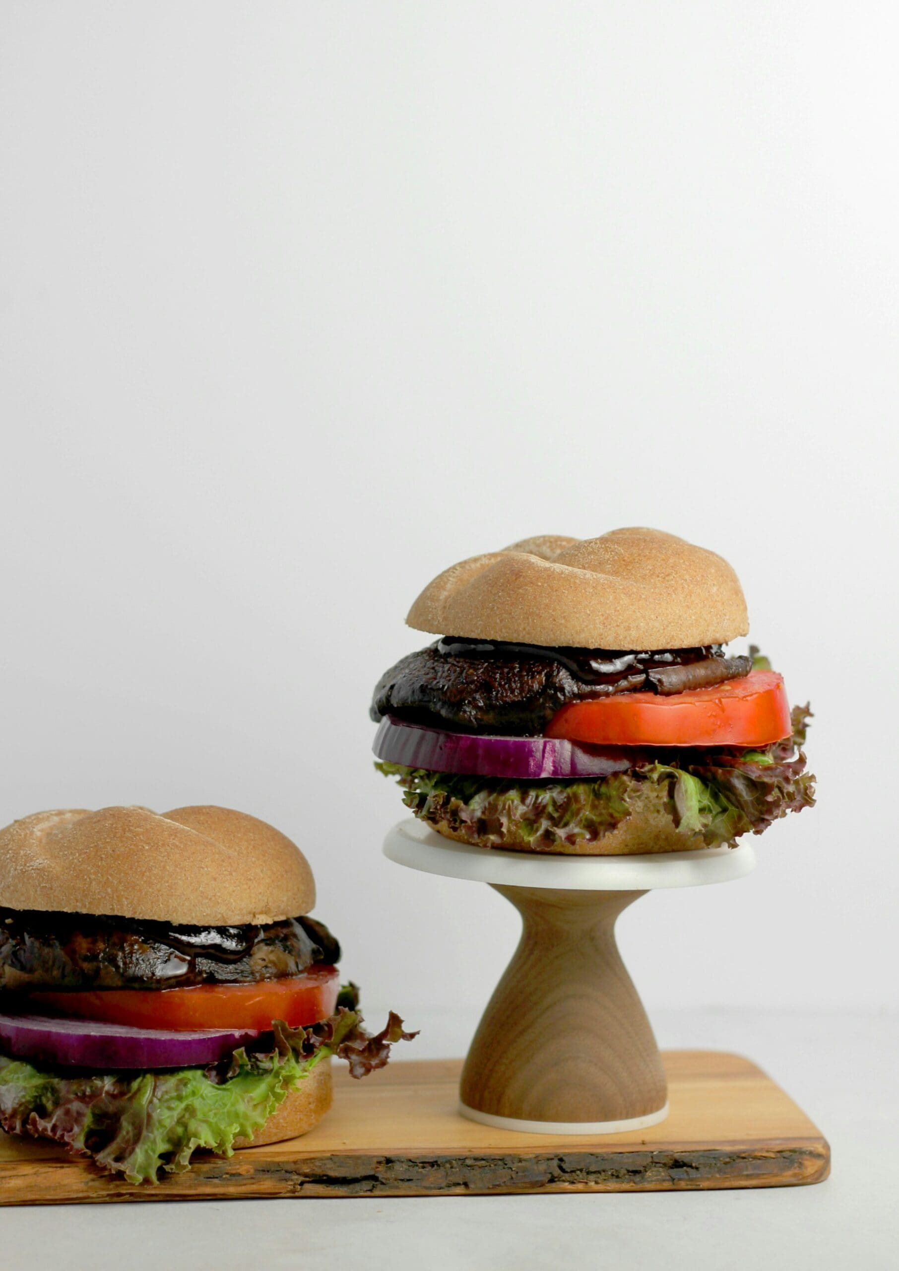 Three plant-based burgers with black portobello patties, stacked with fresh vegetables, on wooden stands.