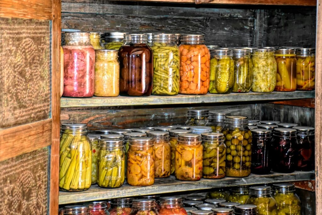 Wooden shelves filled with various jars of canned vegetables, including pickles and beets.