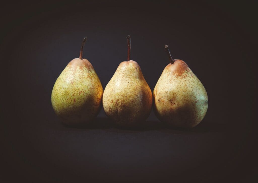 Three ripe pears lined up against a dark backdrop, highlighting their textured skins and natural tones.