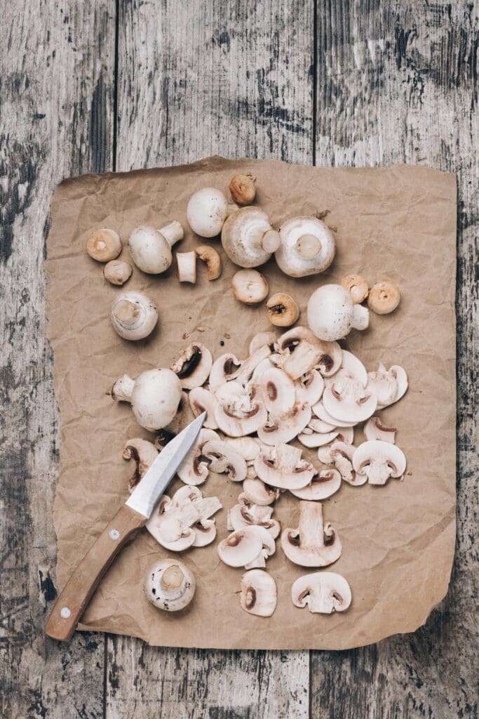Freshly chopped white button mushrooms spread on a rustic wooden background with a vintage kitchen knife.